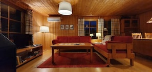 Ein gemütliches Blockhaus-Interieur mit Holzbalkendecke, einem roten Sofa, einem Holzesstisch und einem Fernseher auf einem Holzschrank.
