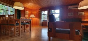 Ein Holzinterieur mit Esstisch und Stühlen, einer Couch und großen Fenstern.