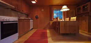 A wooden interior with a kitchen, dining area, and a red rug.
