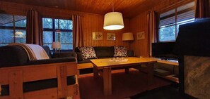 L’intérieur d’un chalet chaleureux, avec une table à manger en bois, un canapé et un téléviseur.