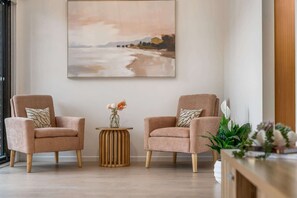 Ein Zimmer mit zwei Sesseln, einem kleinen Holztisch und einem Bild an der Wand.