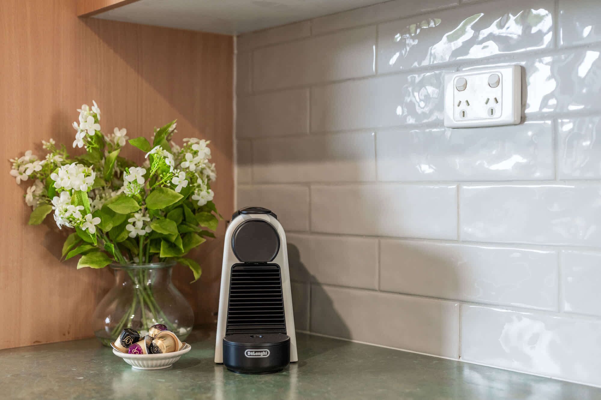 Ein tragbarer DeLonghi-Heizkörper auf einer Küchenarbeitsplatte neben einer Blumenvase und einer Schale mit Pralinen.