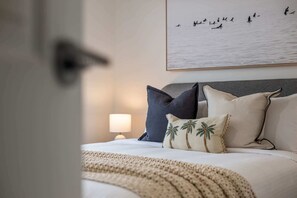 A neatly made bed with pillows, a lamp, and a framed picture of birds on the wall. - Coastal family home - 4BR, walk to beach (Warana)