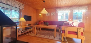 Ein Holzinterieur mit einer Couch, einem Tisch, einem Fernseher und einem Fenster mit Blick auf Bäume.