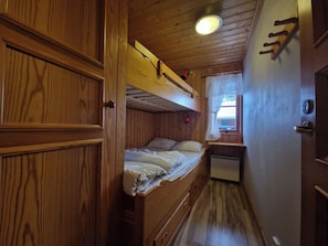 Ein Holzblockhaus-Innenraum mit Etagenbetten, einer kleinen Küchenzeile und einem Fenster mit Vorhängen.