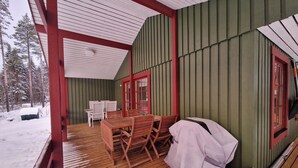 A covered wooden deck with a table and chairs, a covered window, and a snow-covered ground. - Sauna | Wi-Fi | Terrace | Wood stove | Cable TV (Lofsdalen)