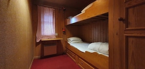 Ein kleines Zimmer im Blockhausstil mit einem Etagenbett, einem kleinen Schreibtisch und einem Fenster mit Vorhängen.