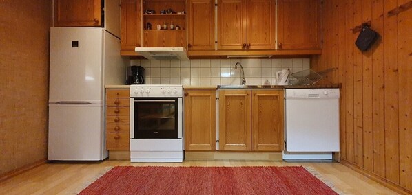Eine kleine Küche mit Holzschränken, einem weißen Kühlschrank, einem Backofen, einer Spüle und einem Geschirrspüler.