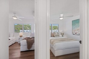Ein Schlafzimmer mit einem Bett, einem Nachttisch, einem Fenster mit Jalousien, einem Deckenventilator und einem Bild an der Wand.