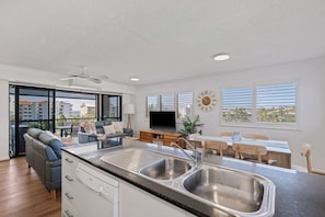 Eine moderne Küche mit Einbauherd, ein Essbereich mit Tisch und Stühlen sowie ein Wohnbereich mit Sofa und Fernseher.