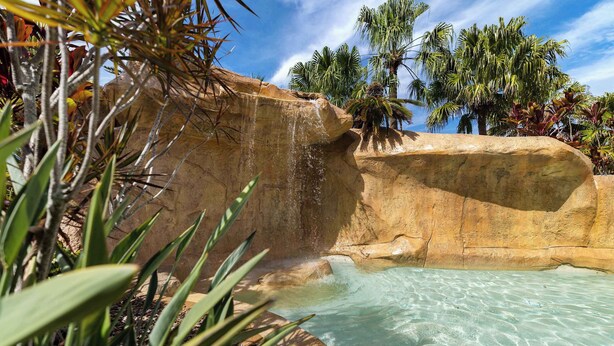 Een natuurlijke rotsformatie met een helder zwembad en een waterval.