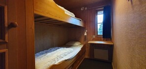 Ein kleiner, kompakter Raum mit Etagenbett, Schreibtisch und Fenster.
