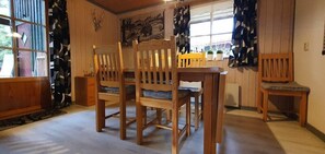 Ein Essbereich mit Holzkstühlen und einem Tisch, ein Fenster mit Vorhängen sowie eine Wand mit einem aufgehängten Tierkopf.