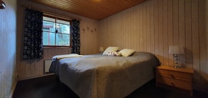 Ein Schlafzimmer mit Bett, Nachttisch, Lampe und einem Fenster mit Vorhängen.
