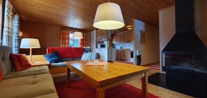 A cozy living room with a wooden table, sofa, and a fireplace. - Sauna | Wi-Fi | Terrace | Wood stove | Cable TV (Lofsdalen)