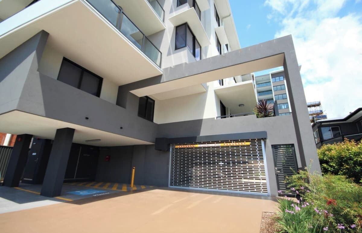 A multi-story building with a modern architectural design, featuring balconies, large windows, and a gated entrance.