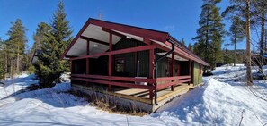 Eine Hütte mit roter Fassade, einer Holzdachterrasse und einer verschneiten Landschaft.