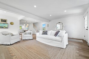 A spacious living room with a white sofa, two white armchairs, a large rug, and a staircase leading to another level.