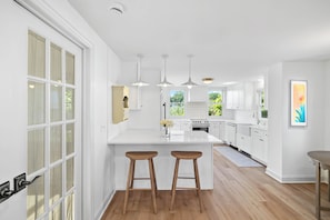 A modern kitchen with white cabinetry, a central island with stools, pendant lighting, and a view of the outdoors.
