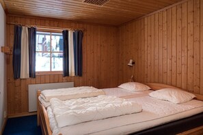 Ein Zimmer mit Holzwänden, zwei Betten, einem mit Vorhängen versehenen Fenster und einer Wandlampe.