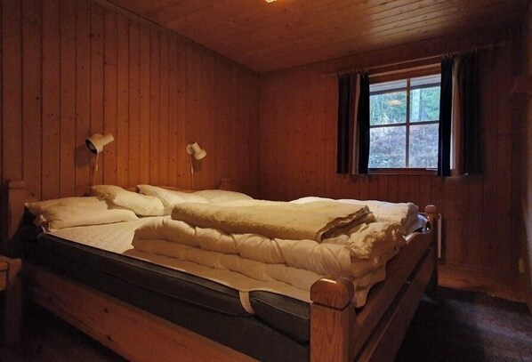 Ein Holzhütten-Zimmer mit einem Einzelbett, zwei Nachttischlampen und einem fenster mit Vorhängen.