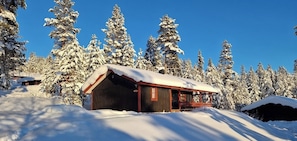 Eine Holzhütte mit schneebedecktem Dach, umgeben von mit Schnee beladenen Bäumen.