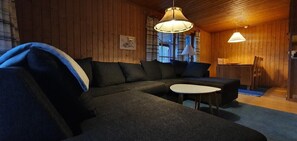 A cozy room with a sectional sofa, a small table, and a dining area with chairs. - Sauna | Wi-Fi | Terrace | Wood stove | Cable TV (Lofsdalen)