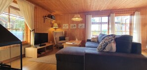 Ein gemütliches Zimmer mit einer Couch, Fernseher, Sessel und einem kleinen Tisch.