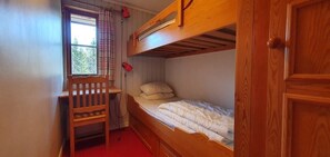 Ein Schlafraum mit Etagenbetten, einem Schreibtisch und Stuhl, einem Fenster mit Vorhängen und einer Tür.