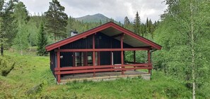 Eine Hütte mit rotem Dach und Holzwänden, umgeben von einem Wald, mit einem Berg im Hintergrund.