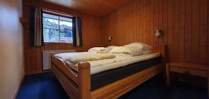 Ein Zimmer mit Holzwandverkleidung, einem Bett, einem Fenster mit Vorhängen und einer Nachttischlampe.