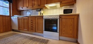 Eine Küche mit Holzschränken, einem Geschirrspüler, einem Backofen, einer Mikrowelle und einem gemusterten Teppich.
