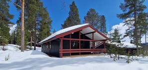 Eine Hütte mit roter Außenfarbe, umgeben von Schnee und Bäumen.