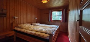 Ein Schlafzimmer einer Holzhütte mit einem Einzelbett, einem Fenster mit Vorhängen und einer Holztür.