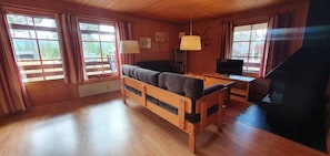 Ein Holzblockhaus-Interieur mit einer Couch, einem Fernseher, einem Kamin und großen Fenstern.