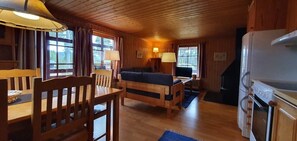 Eine Hütte mit Esstisch, Stühlen, einer Couch, einem Kühlschrank und einem Kamin.