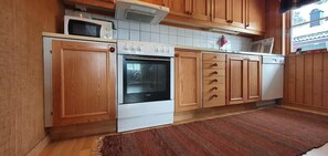 Eine Küche mit Holzausstattung, einer Mikrowelle, einem Backofen und einer gefliesten Spritzschutzwand.