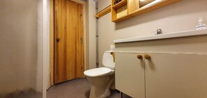 A bathroom with a wooden door, a white toilet, and a white cabinet with wooden knobs.