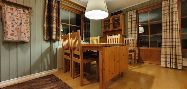 Ein Holztisch mit Stühlen, eine Hängeleuchte und ein Fenster mit Vorhängen.