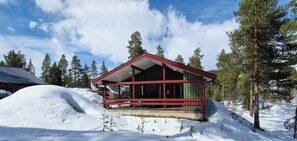 A cabin with a red roof and a porch, surrounded by snow and trees.