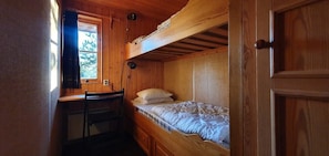 Eine Holzhütte mit einem Etagenbett, einem Schreibtisch und einem Fenster mit Vorhängen.