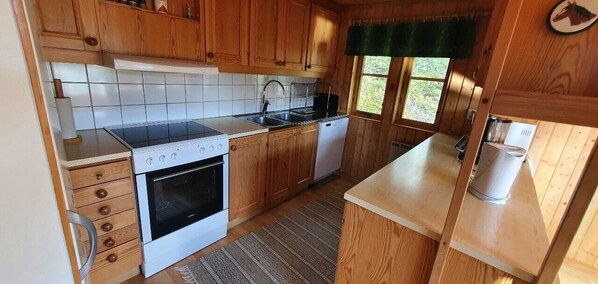 A kitchen with wooden cabinets, a stove, a dishwasher, and a window with a view of greenery. - Sauna | Wi-Fi | Terrace | Wood stove | Cable TV (Lofsdalen)