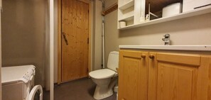 Ein Badezimmer mit Toilette, Holzsärchen, einer Waschmaschine und Ablage für Toilettenartikel.