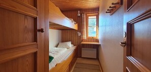 Ein Holzhütten-Innenraum mit Etagenbett, einer kleinen Küchenzeile und einem Fenster mit Blick auf Grünflächen.