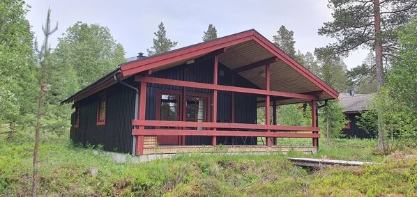 Punakatolla varustettu puinen mökki, jossa on kuisti, ja sen ympärillä on puita.