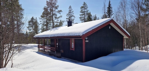 Eine Holzhütte mit einer Veranda, einem mit Schnee bedeckten Dach und blauem Himmel.