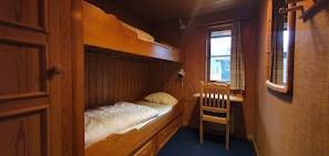 Kerrossänky, jossa alhaalla on yksi sänky, puinen tuoli ja ikkuna, jossa on verhot.