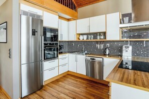 A modern kitchen with stainless steel appliances, wooden flooring, and white cabinetry. - Ski-in/out | Pool table | Sauna | BBQ grill | WiFi (Lofsdalen)