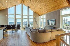 A modern living room with a large sectional sofa, a dining area with chairs, a fireplace, and a TV mounted on a wall. - Ski-in/out | Pool table | Sauna | BBQ grill | WiFi (Lofsdalen)