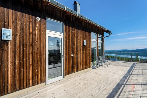 Un edificio de madera con puerta de vidrio, balcón con sillas y vistas al paisaje.